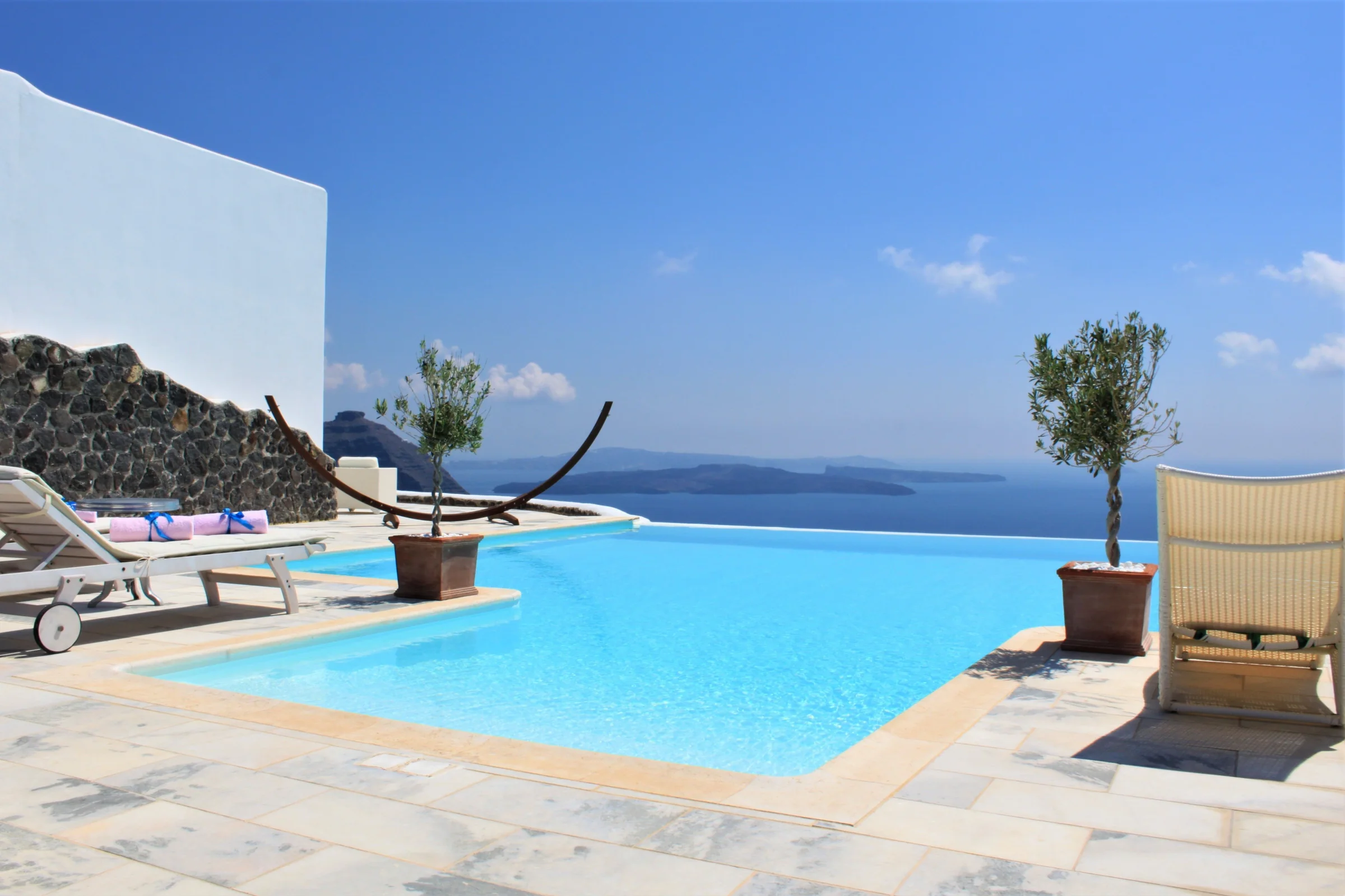 Sunlit infinity pool and white terrace overlooking the Aegean Sea in Santorini, Greece