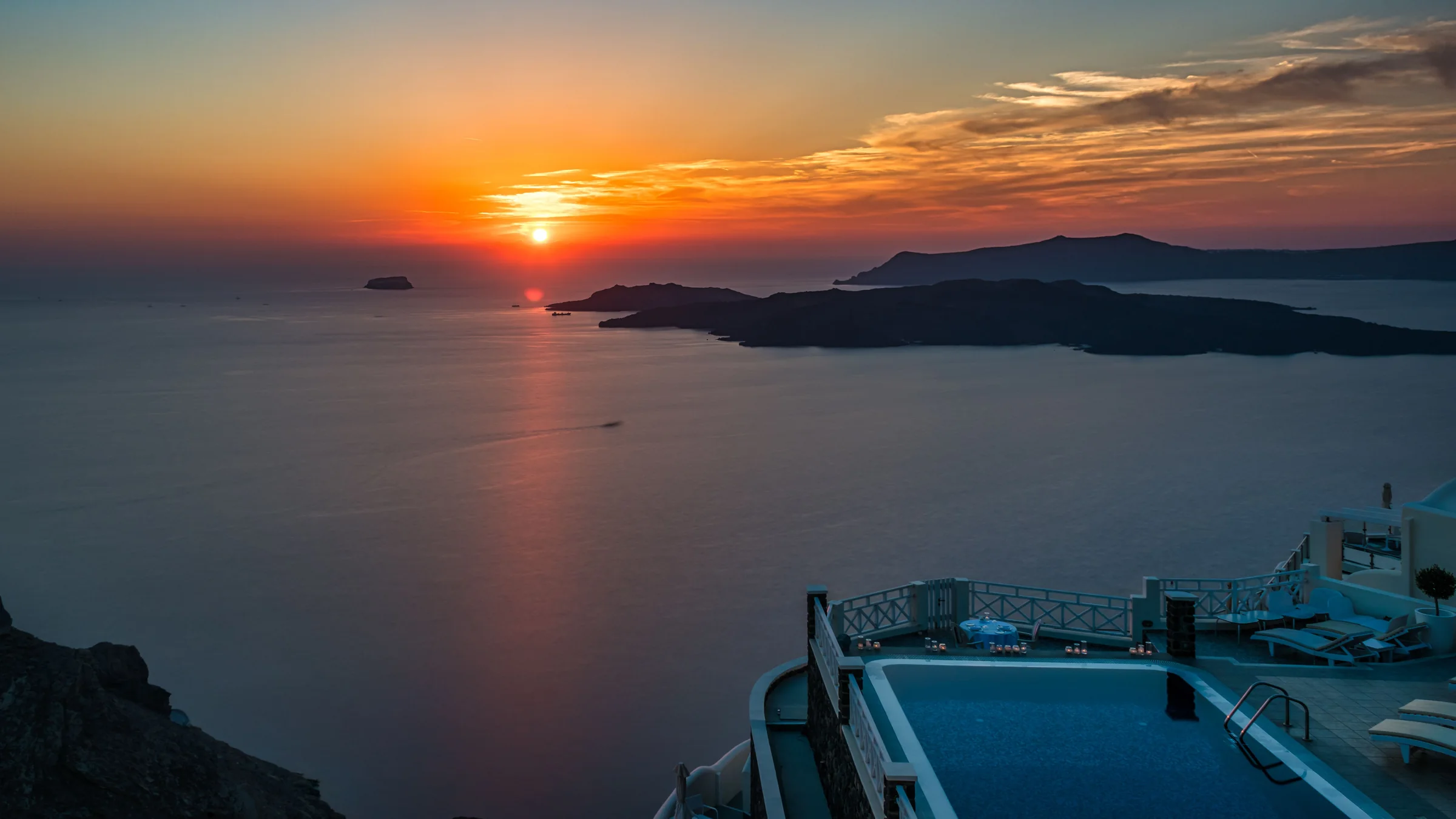 Sunset over the Aegean Sea with a poolside terrace in Santorini, Greece