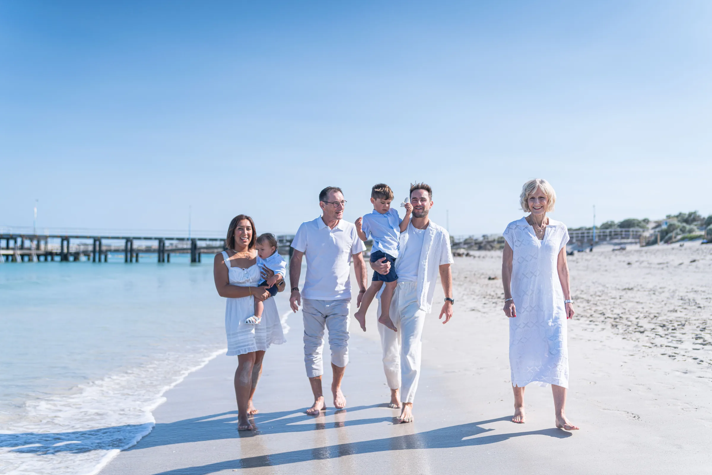 A family of several generations walking together beside the sea on a bright day